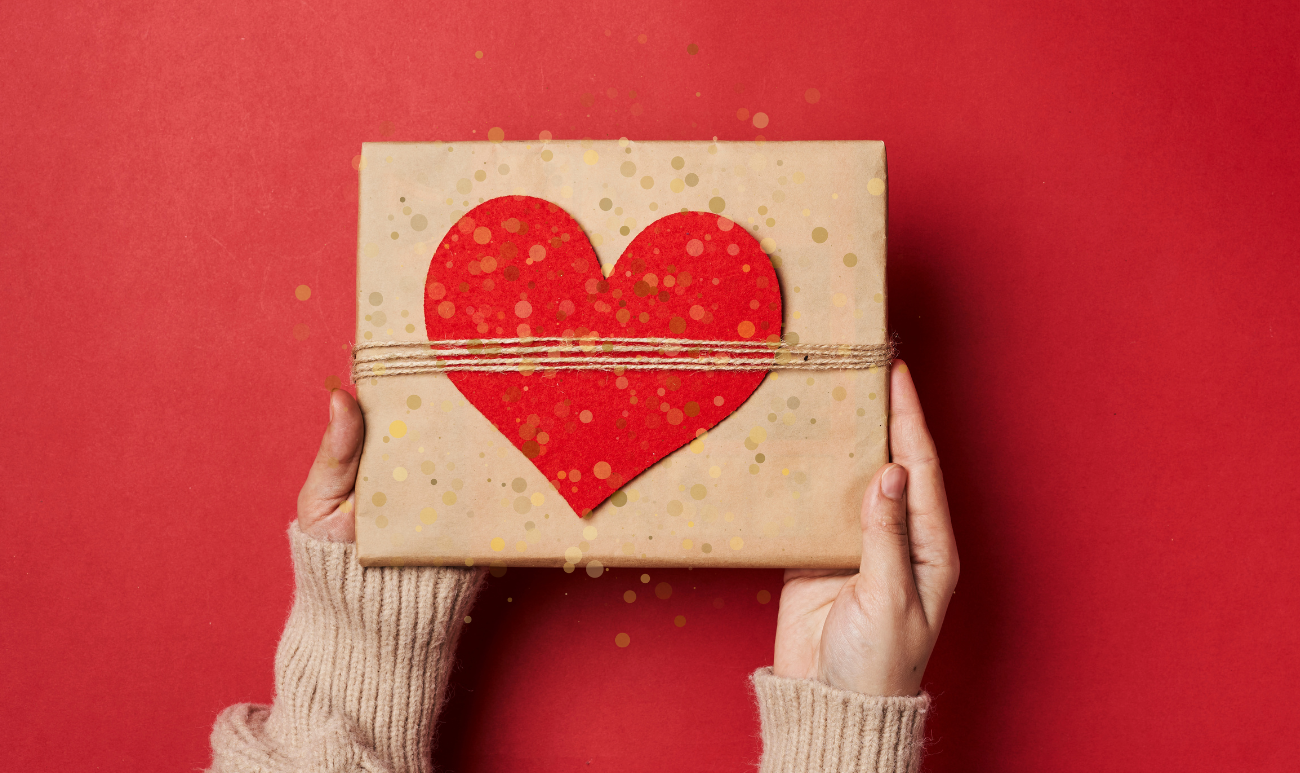 Prezent w brązowym papierze z czerwonym sercem w dłoniach na czerwonym tle – symbol uważnego i pełnego miłości obdarowania