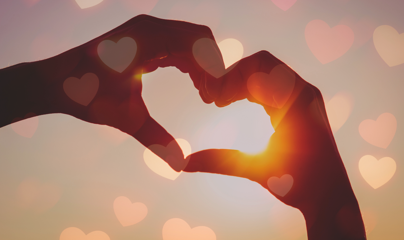 Dłonie tworzące serce na tle zachodzącego słońca – symbol miłości i energii