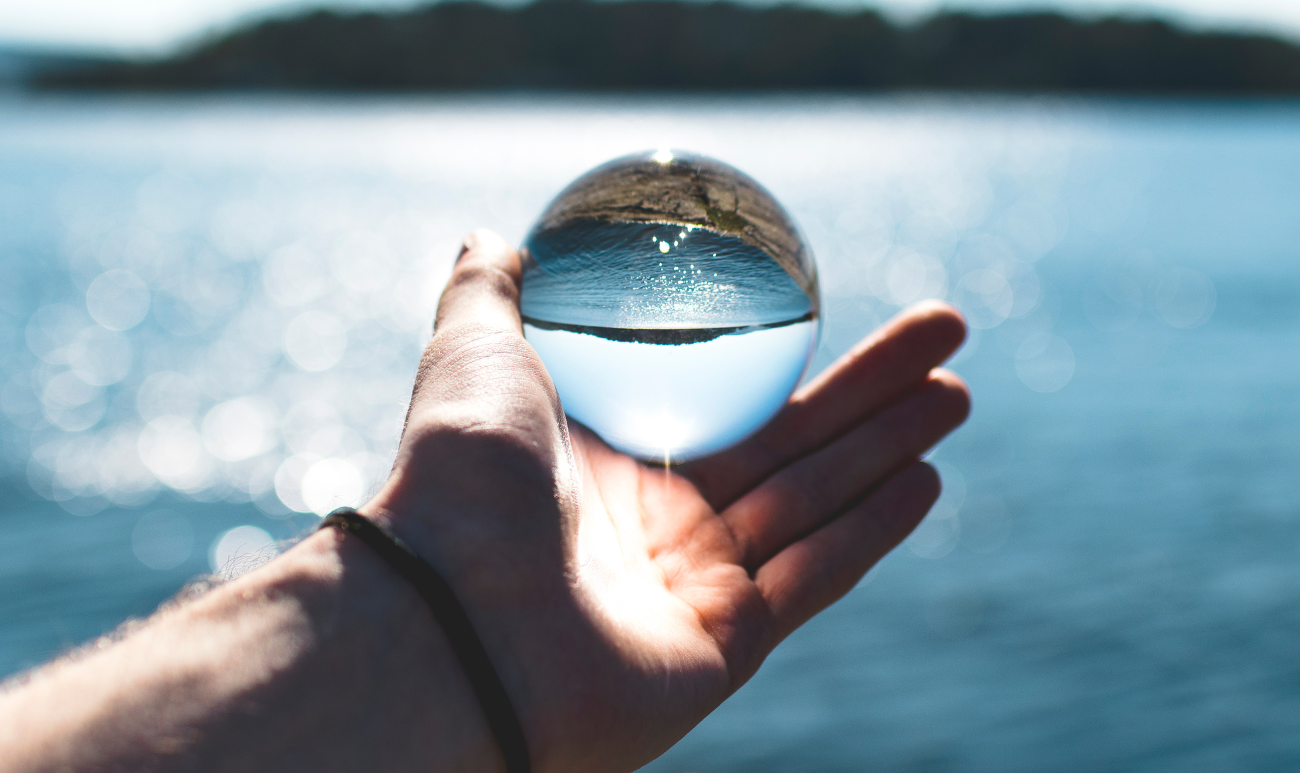 Energetyzacja wody za pomocą świadomości – dłoń trzymająca szklaną kulę nad jeziorem, symbolizująca duchowe połączenie człowieka z naturą i wibracjami.