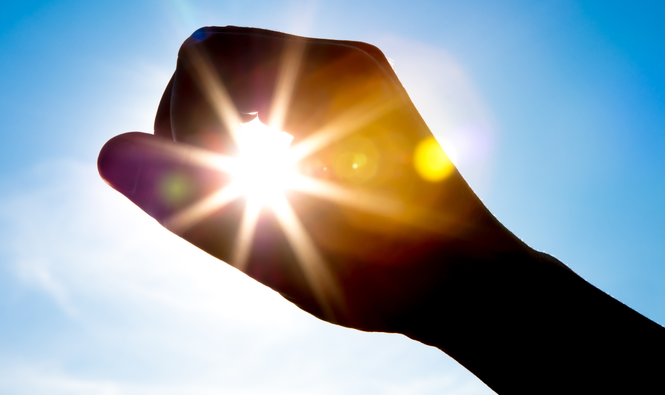 Ręka tworząca okrąg ze słońcem w tle: symbol letniej ochrony biopola i energetycznej higieny aury