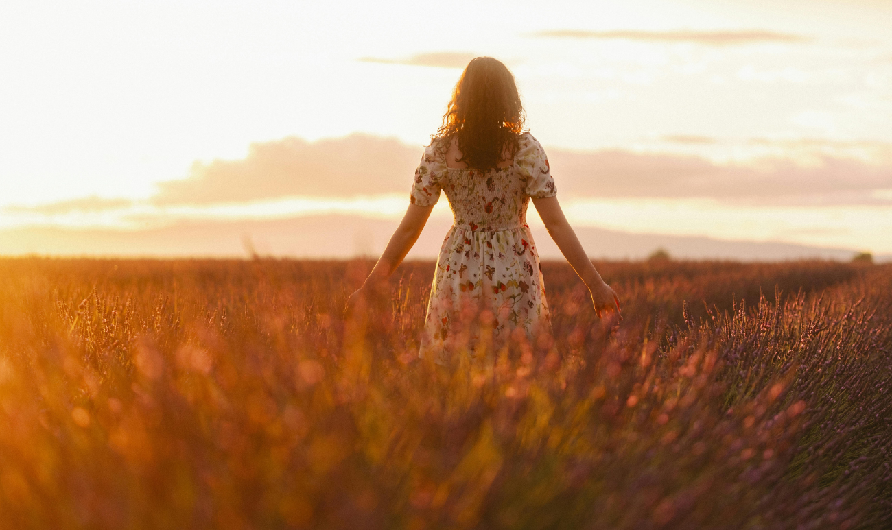 Kobieta w letniej sukience w polu lawendy o zachodzie słońca, symbolizująca letnie przesilenie i duchową transformacja z marką Creatoz.