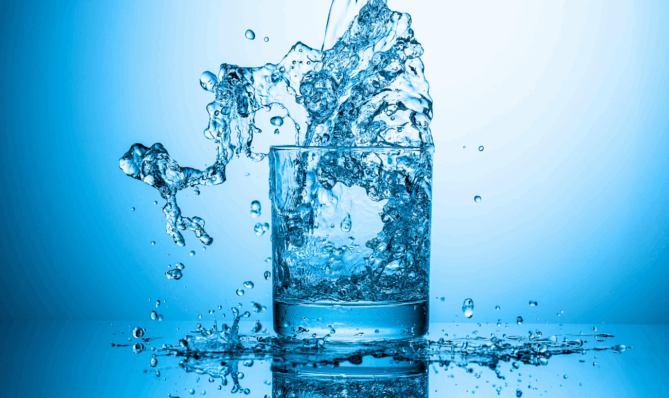 Energetyzowana woda rozpryskująca się w szklance na niebieskim tle symbolizująca świeżość i wysokie wibracje