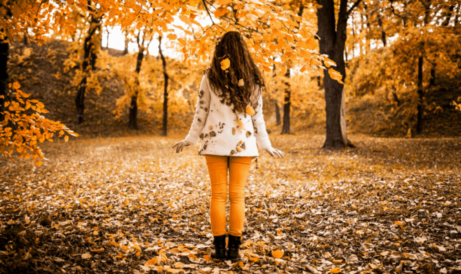 Kobieta w jesiennym parku otoczona złotymi liśćmi – symbol odpuszczania i transformacji zastanawia się jak jesienią psychosomatyka pokazuje jej wewnętrzną prawdę