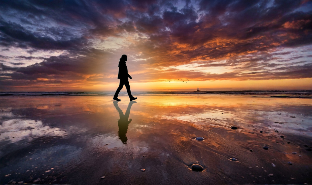 sylwetka człowieka spacerującego po plaży o zachodzie słońca z odbiciem w wodzie symbolizująca aurę i wewnętrzne czucie